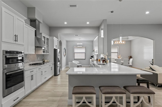 kitchen featuring light hardwood / wood-style floors, appliances with stainless steel finishes, white cabinets, decorative light fixtures, and backsplash