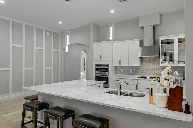 kitchen featuring white cabinetry, light wood-type flooring, pendant lighting, wall chimney exhaust hood, and sink