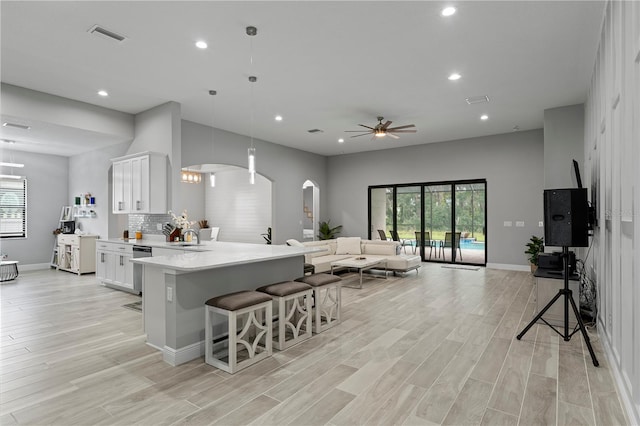 kitchen featuring decorative light fixtures, light hardwood / wood-style floors, ceiling fan, white cabinets, and a breakfast bar