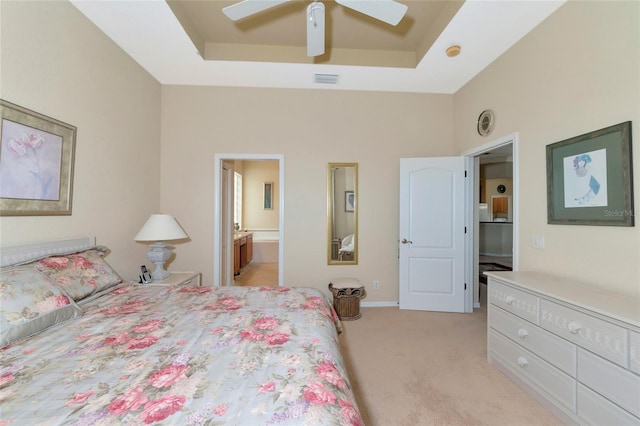 bedroom featuring light carpet, ensuite bathroom, ceiling fan, and a raised ceiling