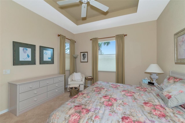 carpeted bedroom with a tray ceiling, ceiling fan, and multiple windows