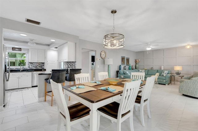 dining area with ceiling fan with notable chandelier, a tray ceiling, and sink