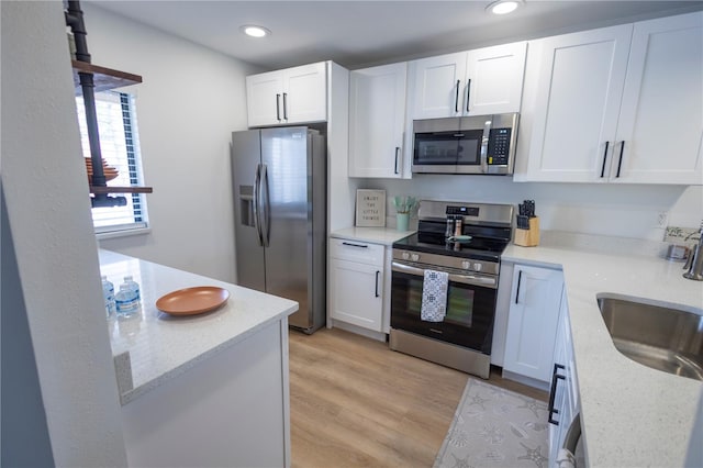 kitchen featuring stainless steel appliances, white cabinetry, light hardwood / wood-style floors, and sink