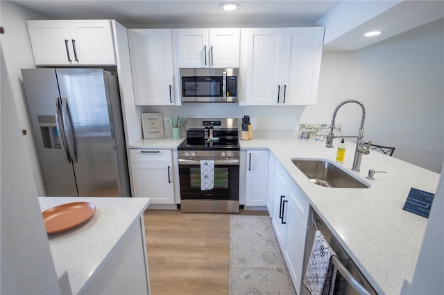 kitchen with sink, light stone countertops, appliances with stainless steel finishes, light hardwood / wood-style floors, and white cabinetry