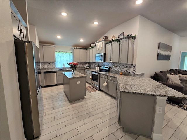 kitchen with a breakfast bar, gray cabinetry, stainless steel appliances, a kitchen island, and vaulted ceiling