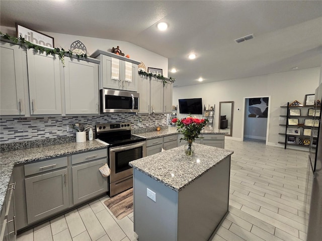 kitchen with gray cabinets, stainless steel appliances, tasteful backsplash, light stone counters, and a kitchen island