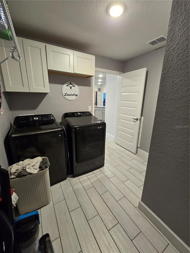 clothes washing area featuring cabinets, independent washer and dryer, and a textured ceiling