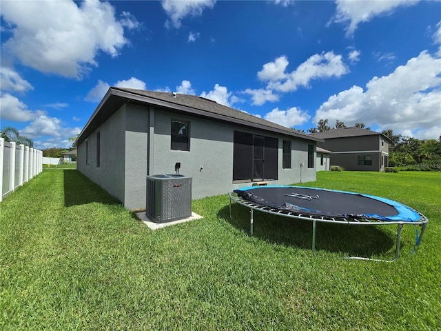 back of house with a trampoline, cooling unit, and a yard