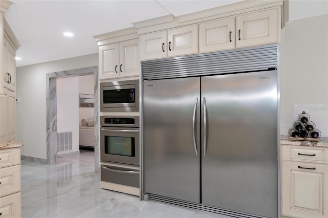 kitchen featuring built in appliances, light stone countertops, and cream cabinets