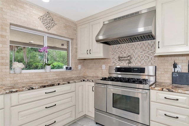 kitchen featuring backsplash, white cabinets, stainless steel range with gas cooktop, wall chimney range hood, and light stone counters