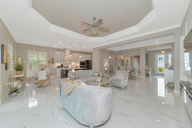 living room featuring a tray ceiling, a healthy amount of sunlight, ceiling fan with notable chandelier, and ornamental molding