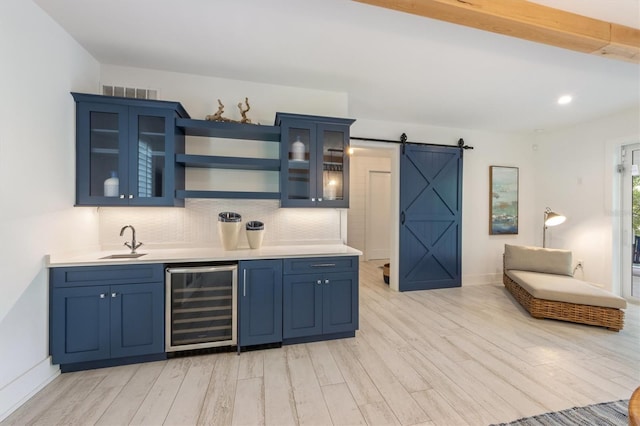 kitchen featuring a barn door, wine cooler, blue cabinets, tasteful backsplash, and light hardwood / wood-style flooring