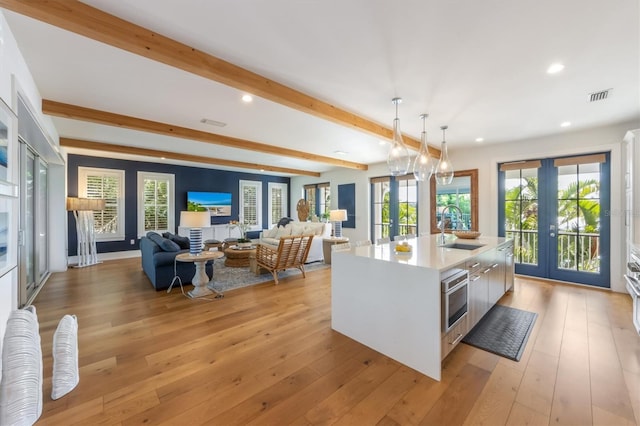 kitchen with french doors, a kitchen island with sink, light hardwood / wood-style floors, sink, and white cabinets