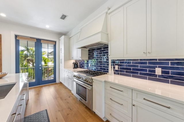 kitchen featuring light wood-type flooring, backsplash, premium range hood, white cabinets, and stainless steel stove