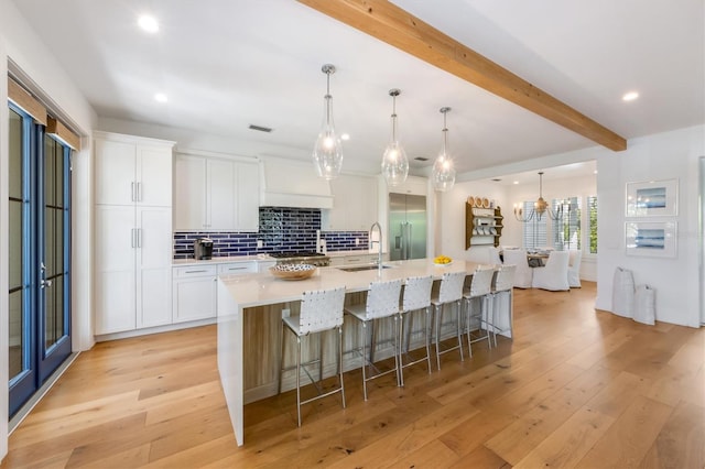 kitchen with beamed ceiling, a large island with sink, light hardwood / wood-style floors, and white cabinetry