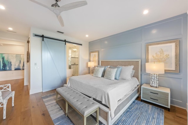 bedroom with ceiling fan, connected bathroom, a barn door, and hardwood / wood-style flooring