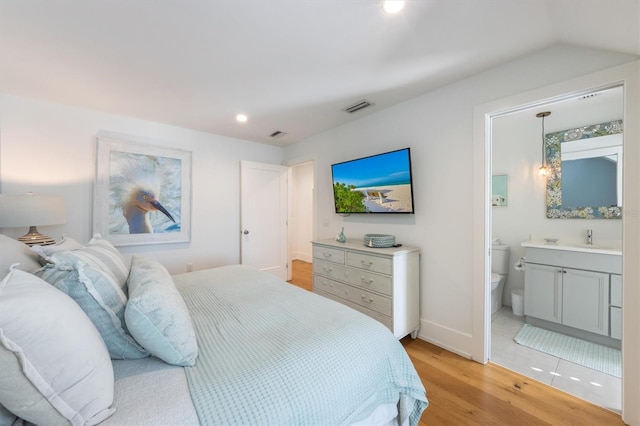 bedroom with ensuite bath, light hardwood / wood-style flooring, and vaulted ceiling