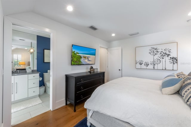 bedroom featuring ensuite bath, hardwood / wood-style floors, lofted ceiling, and sink