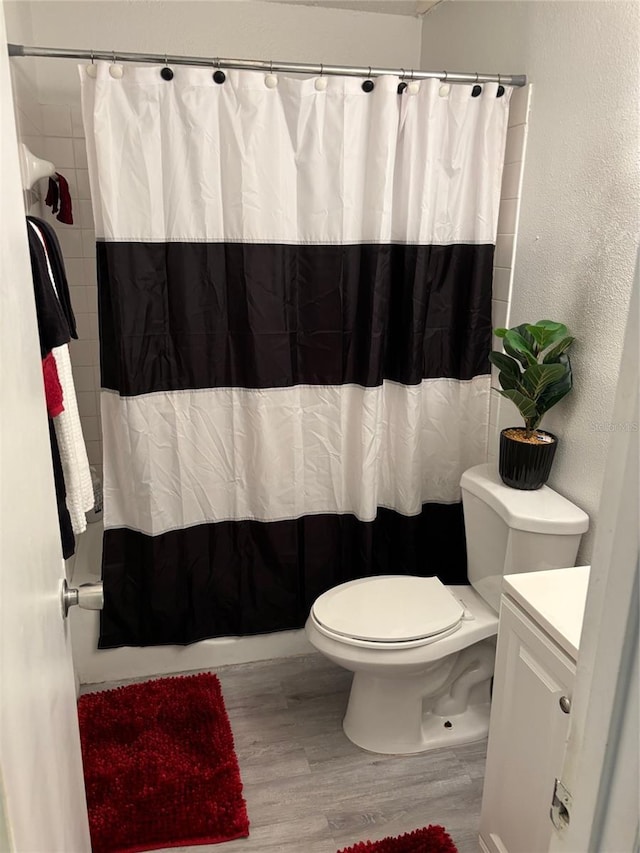 bathroom with a textured wall, shower / bathtub combination with curtain, toilet, vanity, and wood finished floors