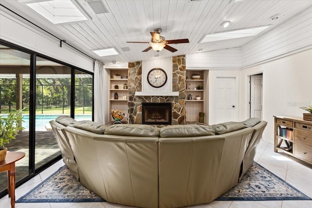 tiled living room featuring lofted ceiling with skylight, ceiling fan, built in features, wooden ceiling, and a stone fireplace