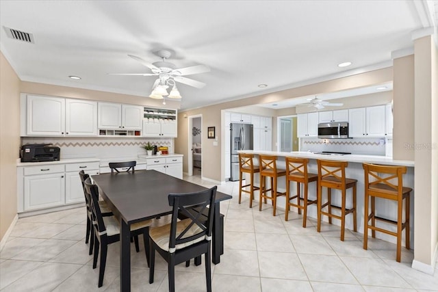 tiled dining area with ceiling fan and ornamental molding