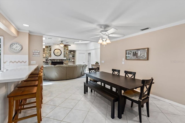 tiled dining space with ceiling fan, ornamental molding, and a fireplace