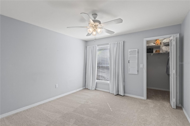 unfurnished bedroom with light carpet, a walk in closet, a closet, and ceiling fan