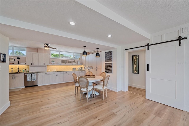 dining space featuring ceiling fan, a barn door, light wood-type flooring, and a textured ceiling