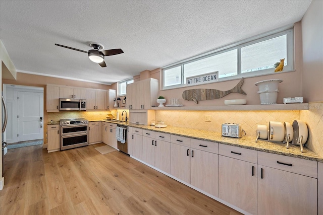 kitchen with sink, light hardwood / wood-style flooring, light stone countertops, tasteful backsplash, and stainless steel appliances