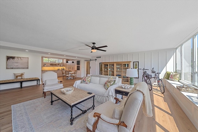 living room with a textured ceiling, a barn door, light hardwood / wood-style flooring, and ceiling fan