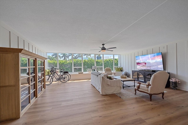 living room with ceiling fan, light hardwood / wood-style floors, and a textured ceiling