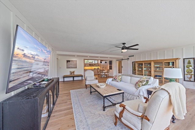 living room featuring ceiling fan, light hardwood / wood-style floors, and a textured ceiling