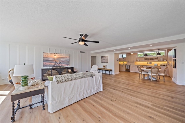 living room with a textured ceiling, light hardwood / wood-style floors, and ceiling fan