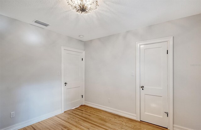 unfurnished room featuring light wood-type flooring, a textured ceiling, and a chandelier