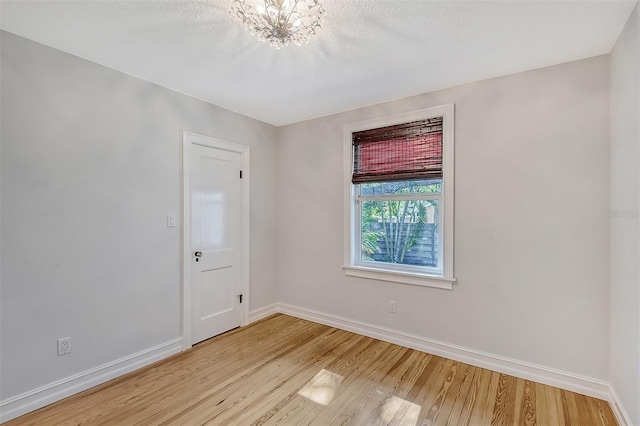 empty room with light hardwood / wood-style floors and an inviting chandelier