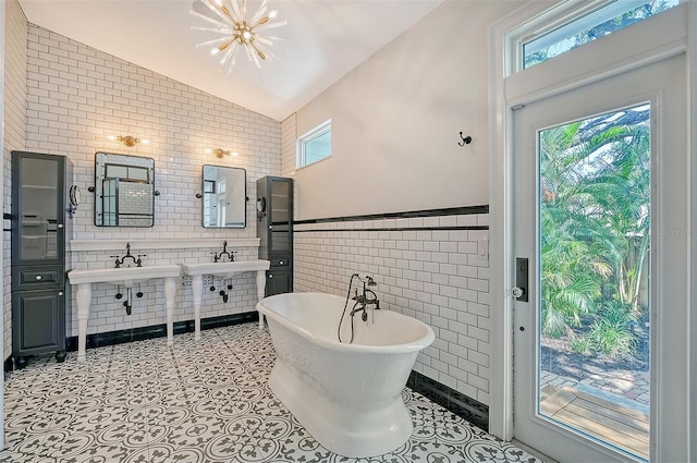 bathroom with a bathtub, an inviting chandelier, sink, vaulted ceiling, and tile walls