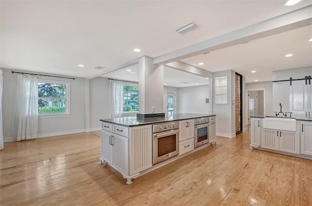 kitchen featuring stainless steel oven, a barn door, white cabinetry, and sink