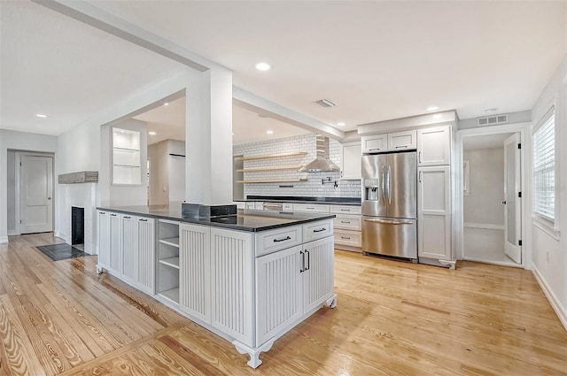 kitchen featuring wall chimney exhaust hood, tasteful backsplash, stainless steel refrigerator with ice dispenser, white cabinets, and light wood-type flooring