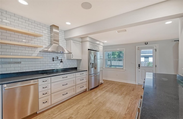 kitchen featuring appliances with stainless steel finishes, backsplash, wall chimney exhaust hood, white cabinets, and light hardwood / wood-style floors