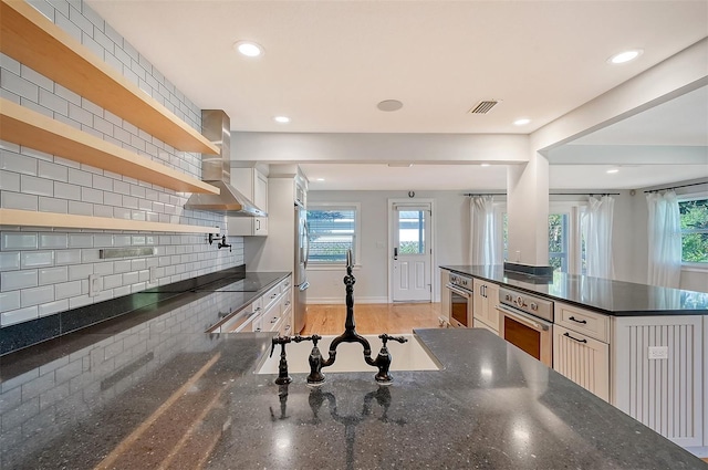 kitchen with backsplash, wall chimney exhaust hood, stainless steel appliances, light hardwood / wood-style flooring, and white cabinets