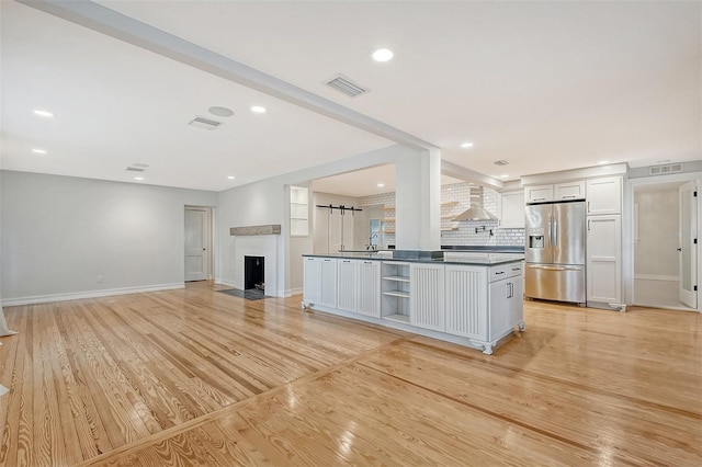 kitchen featuring white cabinets, wall chimney exhaust hood, stainless steel fridge, and light hardwood / wood-style floors