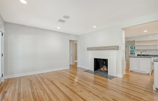 unfurnished living room featuring light hardwood / wood-style flooring, a brick fireplace, and sink