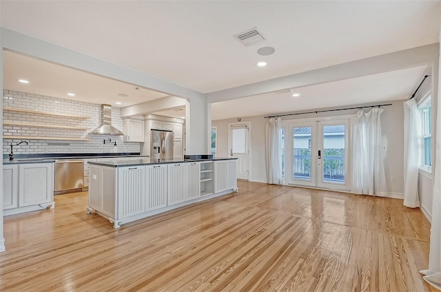 kitchen featuring wall chimney exhaust hood, appliances with stainless steel finishes, tasteful backsplash, light hardwood / wood-style floors, and white cabinetry