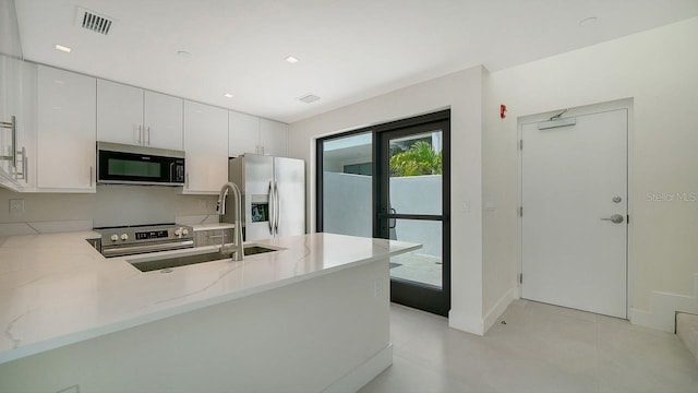 kitchen featuring light stone counters, visible vents, appliances with stainless steel finishes, a sink, and a peninsula