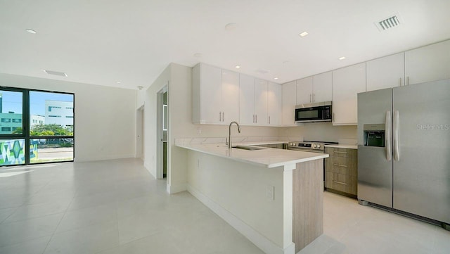 kitchen featuring appliances with stainless steel finishes, kitchen peninsula, white cabinetry, and sink