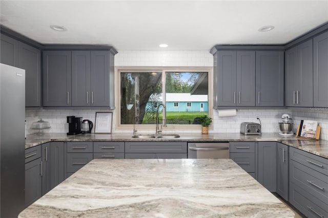 kitchen featuring light stone countertops, appliances with stainless steel finishes, gray cabinets, and sink