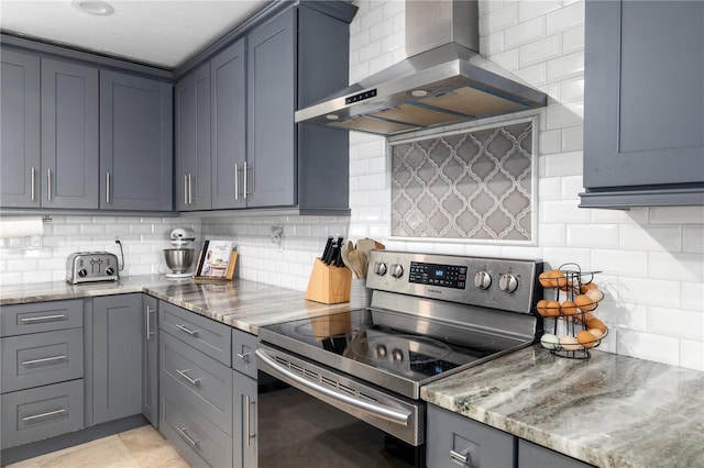 kitchen featuring backsplash, light stone counters, stainless steel electric range oven, and wall chimney range hood