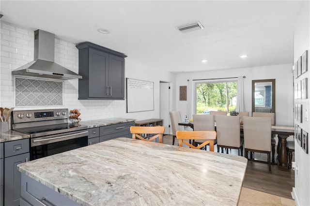 kitchen with light stone countertops, wall chimney range hood, electric range, and visible vents