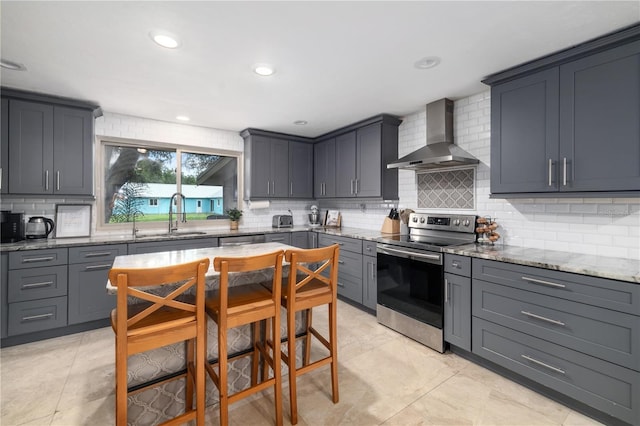 kitchen featuring decorative backsplash, light stone countertops, stainless steel range with electric cooktop, wall chimney range hood, and a sink