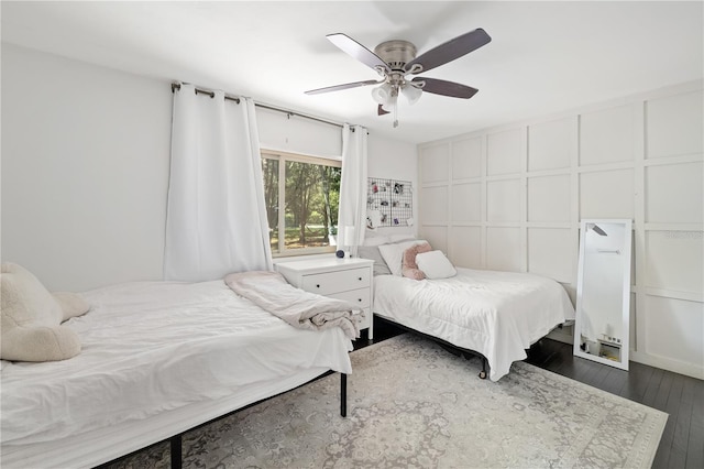 bedroom with dark wood-type flooring, a ceiling fan, and a decorative wall